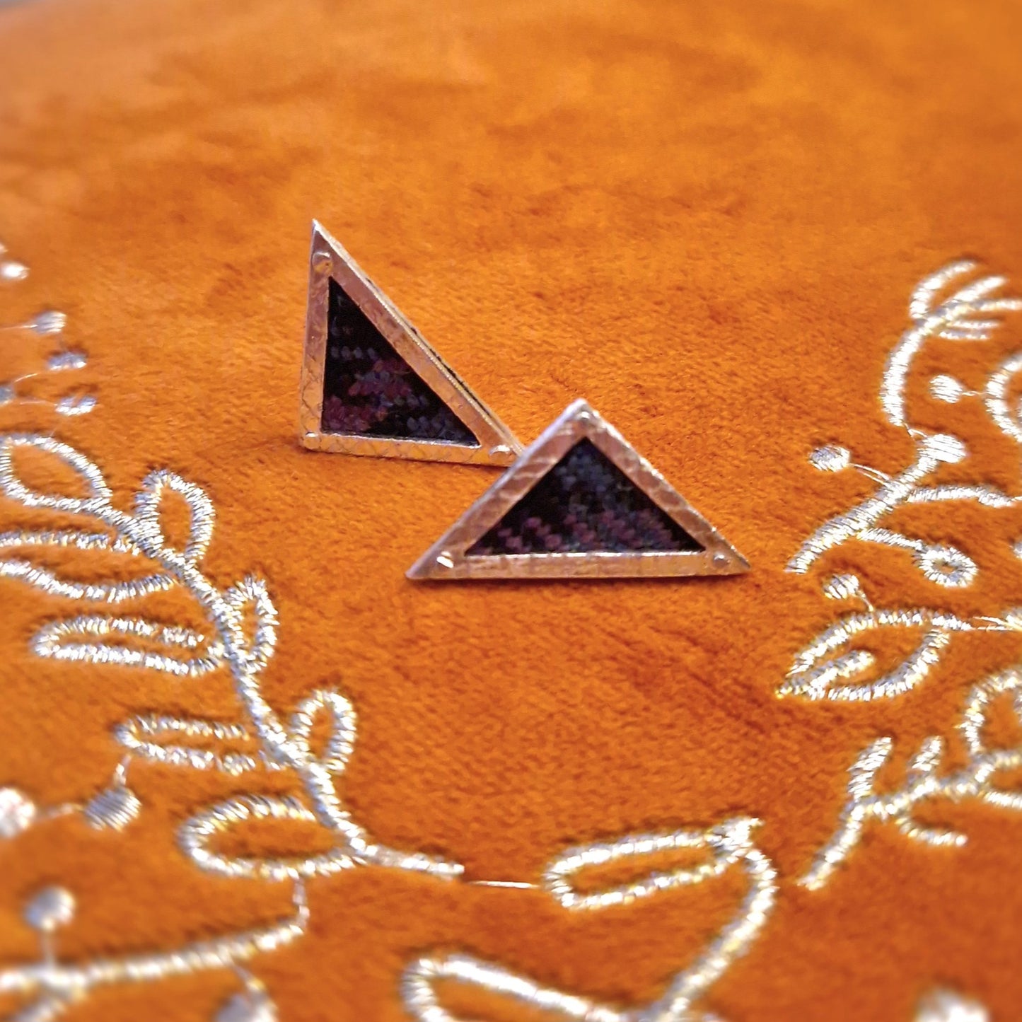 A pair of small, hallmarked sterling silver triangle stud earrings featuring a tartan fabric inlay and secured with sterling silver pins and scrolls.