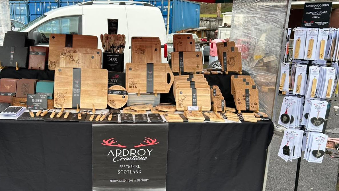 A market stall display for Abroy Handmade, featuring various wooden cutting boards, wooden utensils, and packaged items under a red canopy tent on an outdoor paved surface.