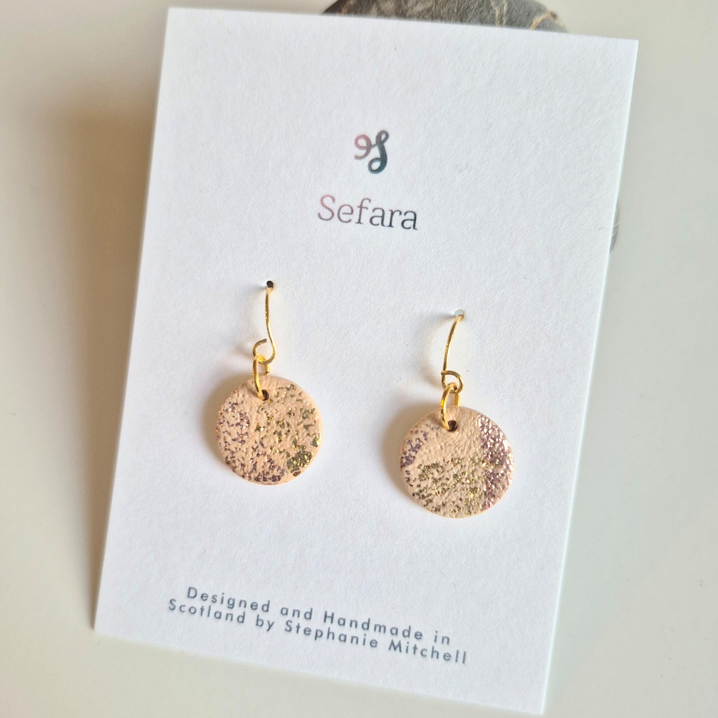 Beige and gold Sefara hook earrings on a branded card