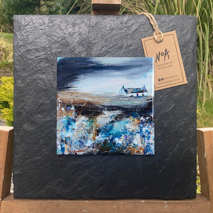 A ceramic tile print of a colourful painting titled 'Bluebells', showing a small house nestled in the Scottish Highlands, available mounted on natural slate or framed.