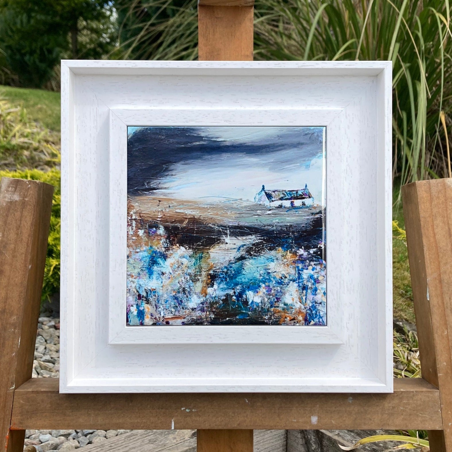 A ceramic tile print of a colourful painting titled 'Bluebells', showing a small house nestled in the Scottish Highlands, available mounted on natural slate or framed.