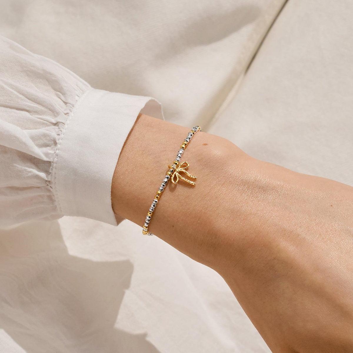 A silver and gold plated Christmas Joma bracelet with a bow charm, packaged in a card that reads 'A Little FA LA LA LA LA'.