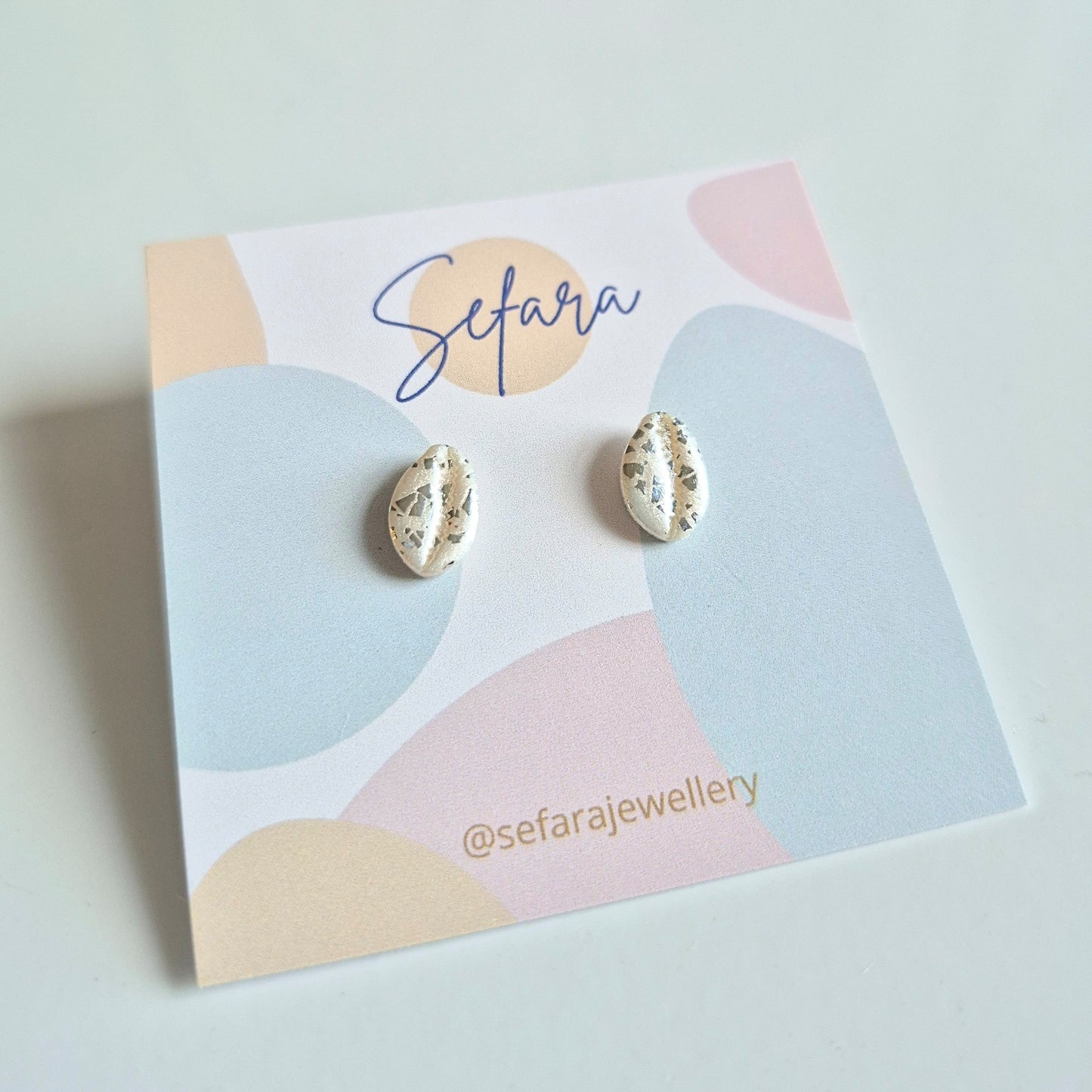 Shell stud earrings with sparkle on a colourful card with 'Sefara' branding.