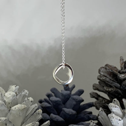 Close-up of a small, round solid sterling silver pendant with a central cut-out heart, approximately 1.2cm in diameter, suspended on an 18-inch silver chain.
