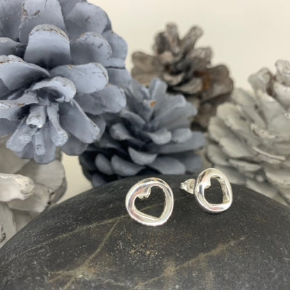 A pair of minimalist solid sterling silver stud earrings with a small, central cut-out heart design, approximately 1.2cm in diameter