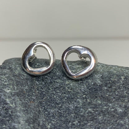 Close-up of a pair of minimalist solid sterling silver stud earrings with a small, central cut-out heart design, approximately 1.2cm in diameter.