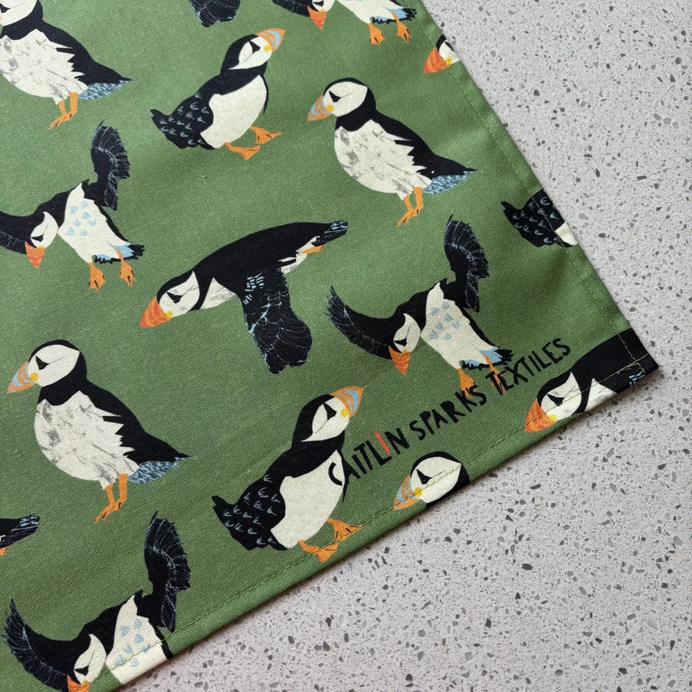 Fabric with puffin pattern and Caitlin Sparks Textiles branding on a green background