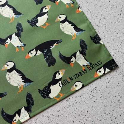 Fabric with puffin pattern and Caitlin Sparks Textiles branding on a green background