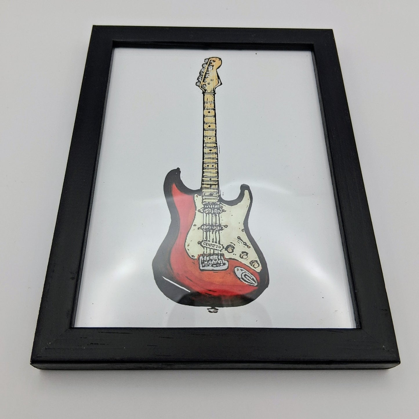 Bee Birds lino print picture of a red and white electric guitar in a small black frame