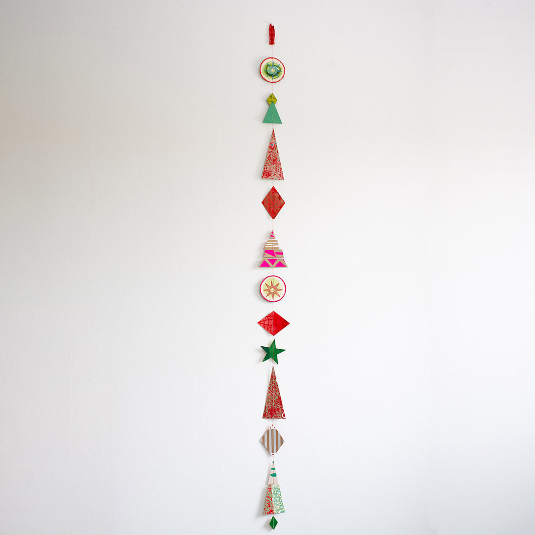 Vertical hanging Christmas garland made of 12 colourful, modern shapes cut from recycled and hand-painted card prints.