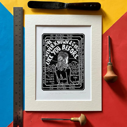 An original black and white linocut print featuring lyrics and imagery inspired by the Edwyn Collins song 'A Girl Like You', mounted on antique white card.