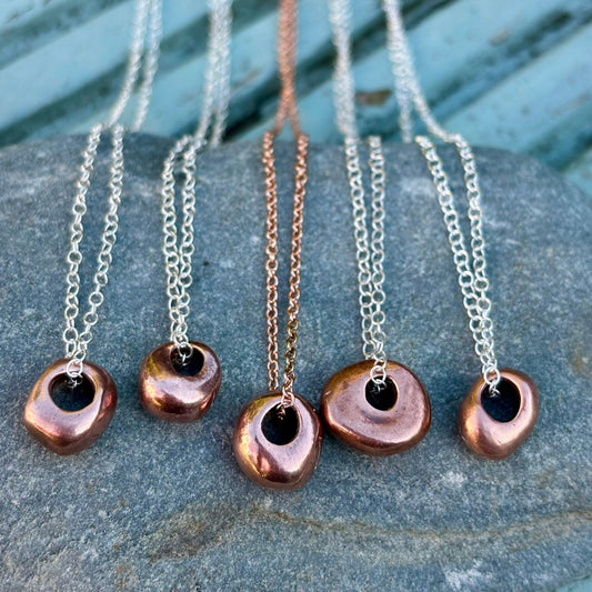 Rowan Berry Jewellery handcrafted solid copper hag stone pendant necklace with a textured, darkened patina, available on an 18-inch sterling silver or rose gold-plated chain.