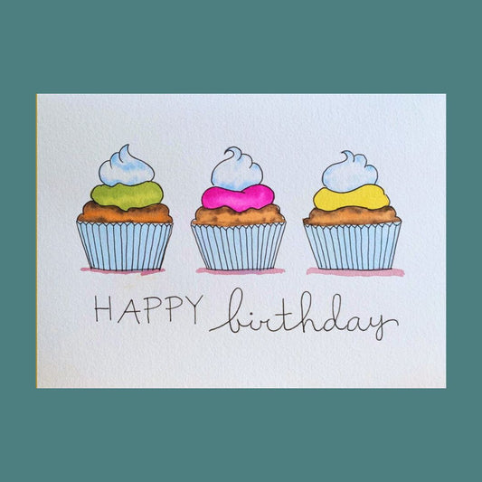 A hand-painted birthday card featuring three colorful cupcakes with the words 'HAPPY birthday' written below them.