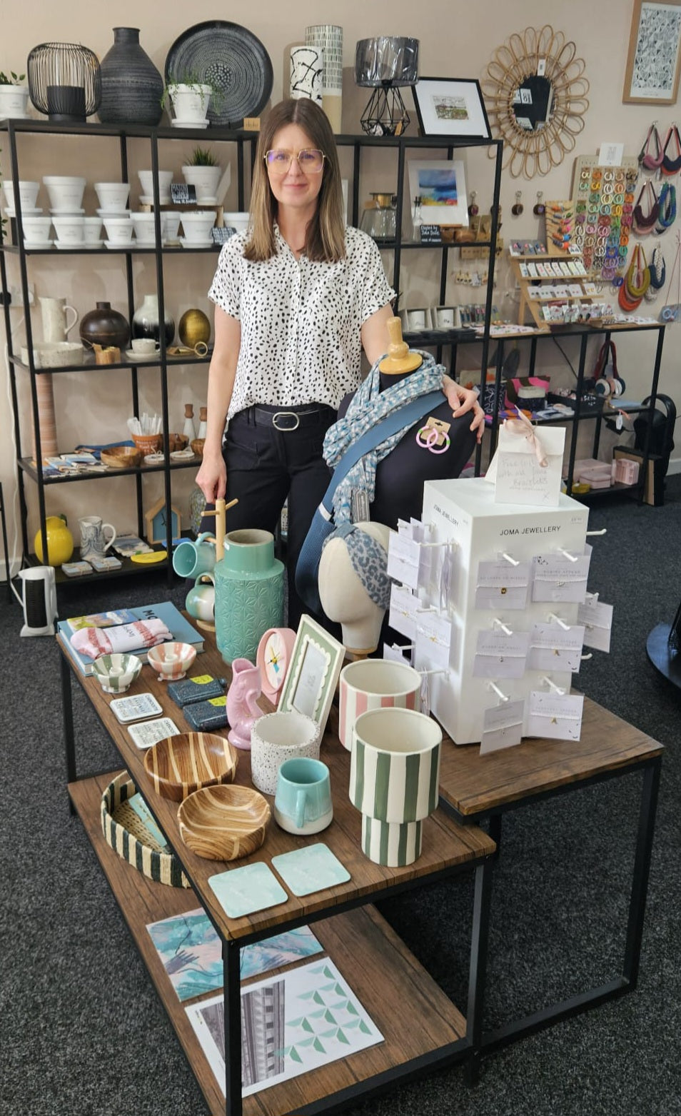 Woman standing behind a table displaying various ceramic items in a store setting.