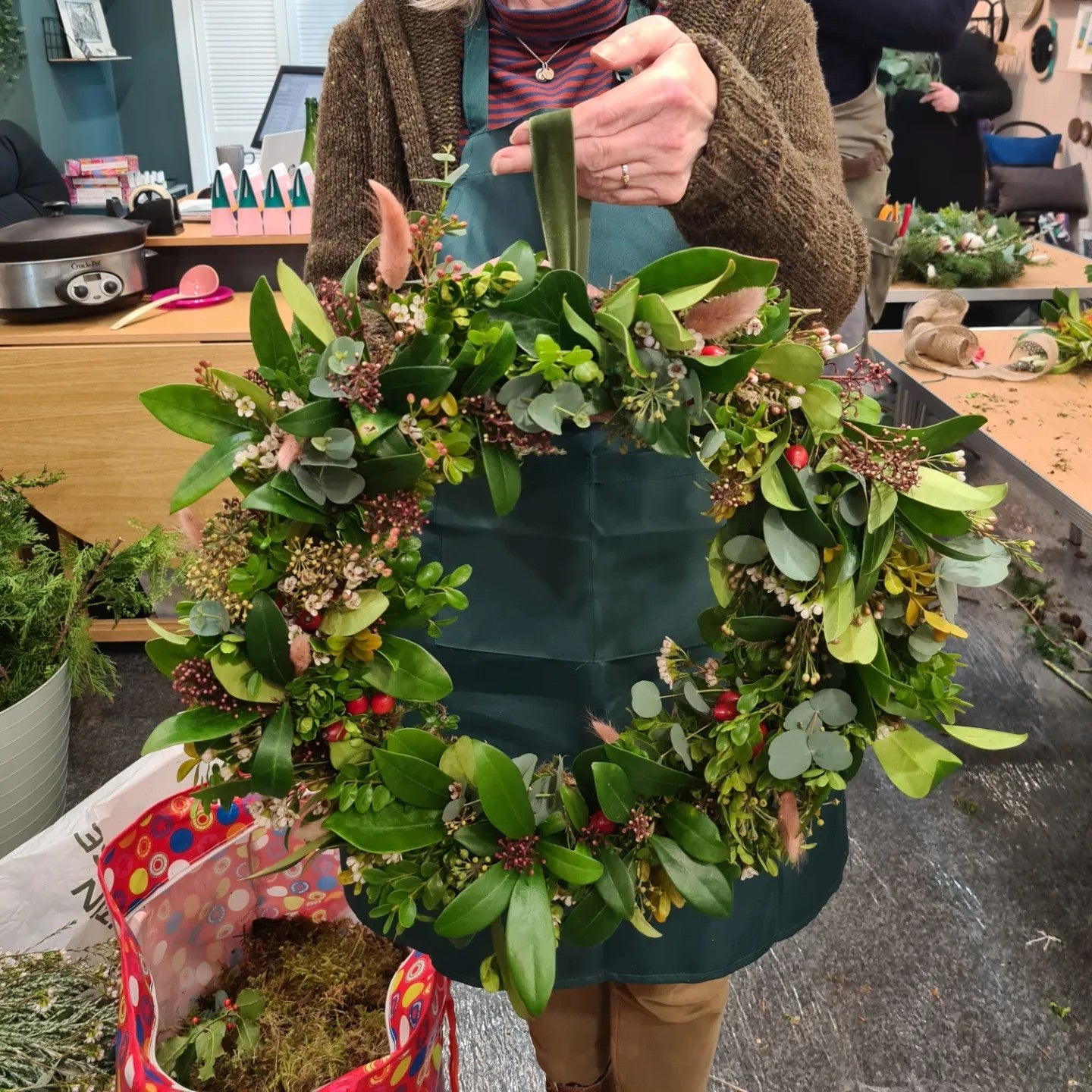 A close-up of a completed wreath with fresh, green foliage and natural decorations on a willow and moss wreath base.