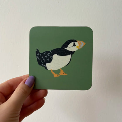 Coaster with puffin design held by a hand against a white background