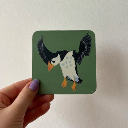 Hand holding a coaster with a puffin design on a plain background