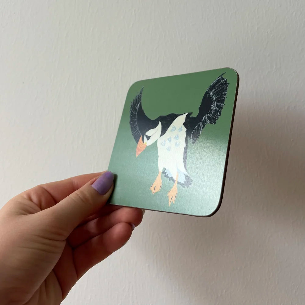 Hand holding a coaster with a puffin design against a plain background