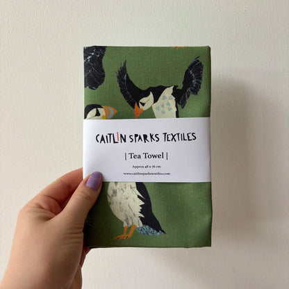 Tea towel with puffin design held by a hand against a plain background