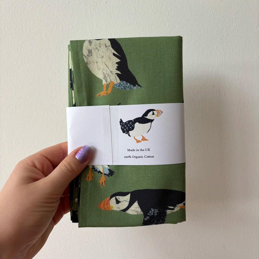 Folded Teatowel with puffin design held by a hand against a plain background