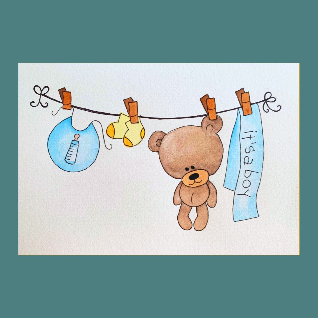 A new baby greeting card featuring a watercolour illustration of a teddy, bib and socks on a washing line with a banner saying 'It's a Boy'