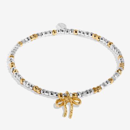 A silver and gold plated Christmas Joma bracelet with a bow charm, packaged in a card that reads 'A Little FA LA LA LA LA'.