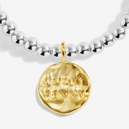 A silver Joma bracelet with a penny charm, packaged in a card that reads 'A Little LUCKY PENNY'.