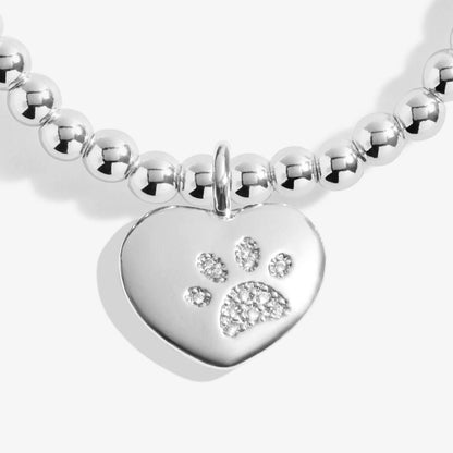 A silver Joma bracelet with a pawprinted heart charm, packaged in a card that reads 'A Little PETS LEAVE PAWPRINTS ON OUR HEARTS'.