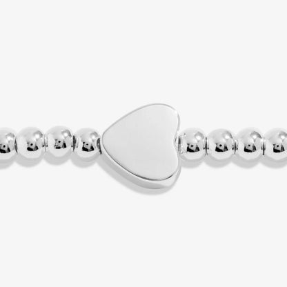 A silver Joma bracelet with a heart charm, packaged in a card that reads 'A Wee BIT O' LOVE'.
