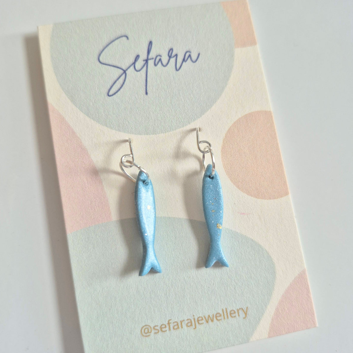 Blue fish-shaped earrings on a colourful card with 'Sefara' branding