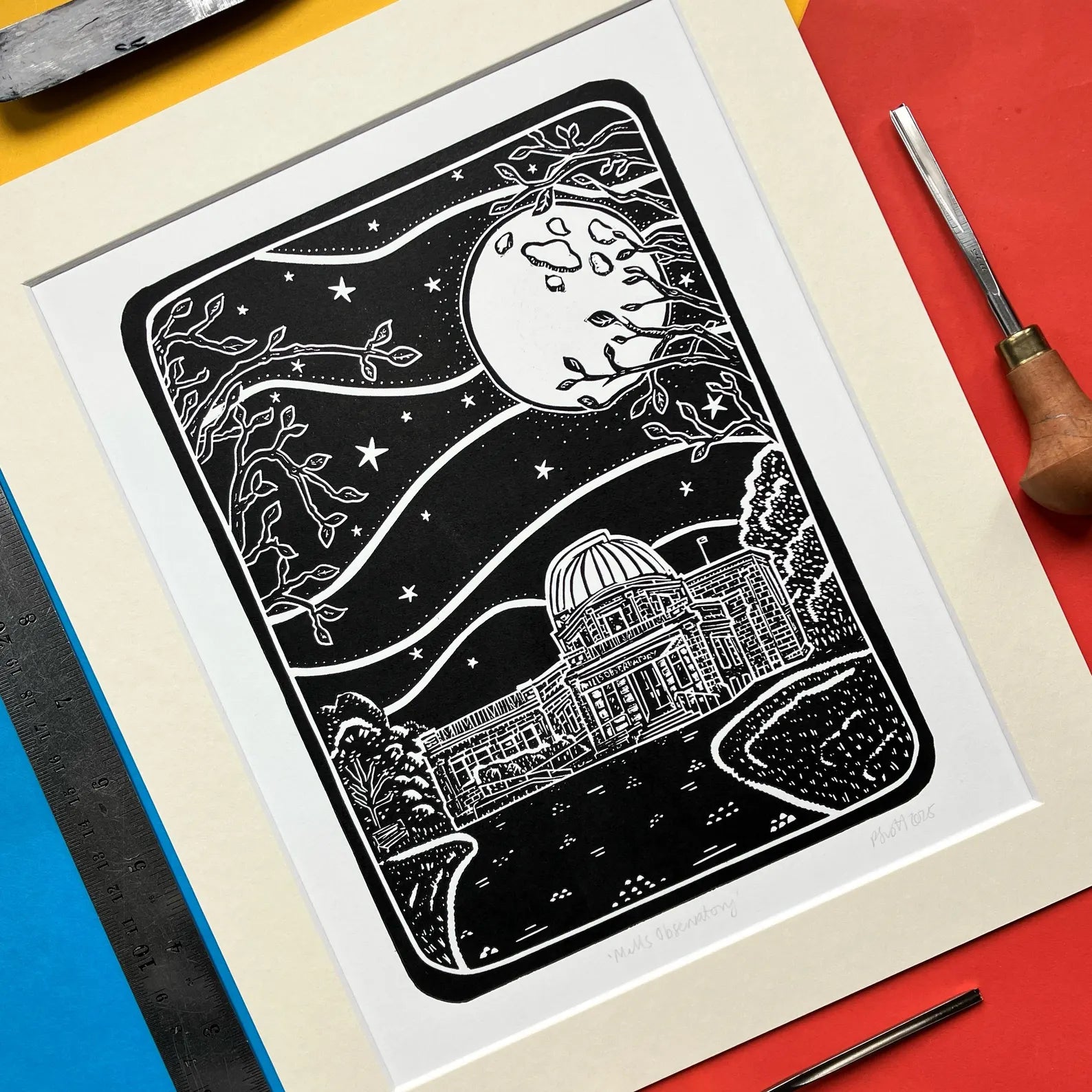 Framed black and white lino print of the Mills Observatory under a moonlit sky, on a colourful background.