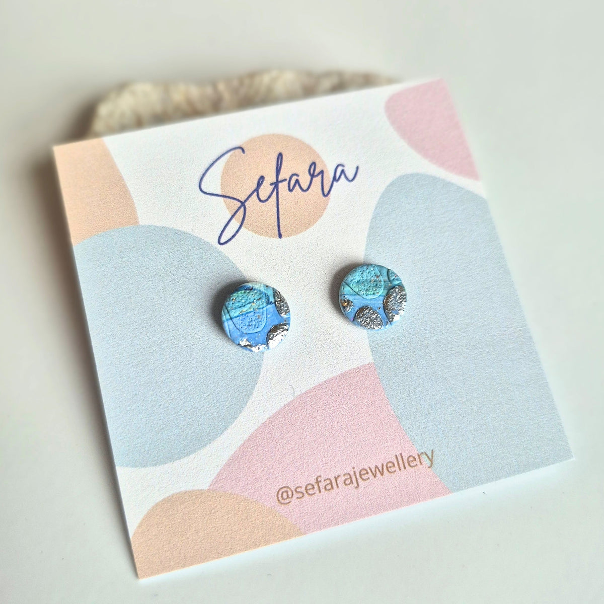 Blue/green round stud earrings with silver accents on a colourful card with 'Sefara' branding