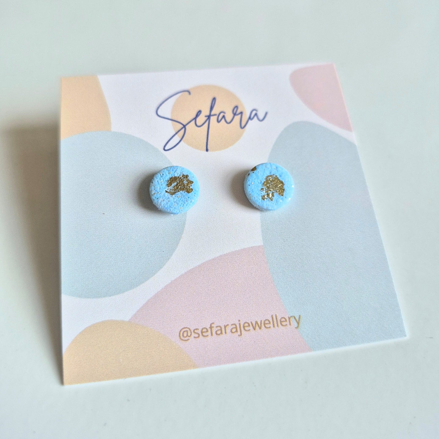 Blue round stud earrings with gold accents on a colourful card with 'Sefara' branding