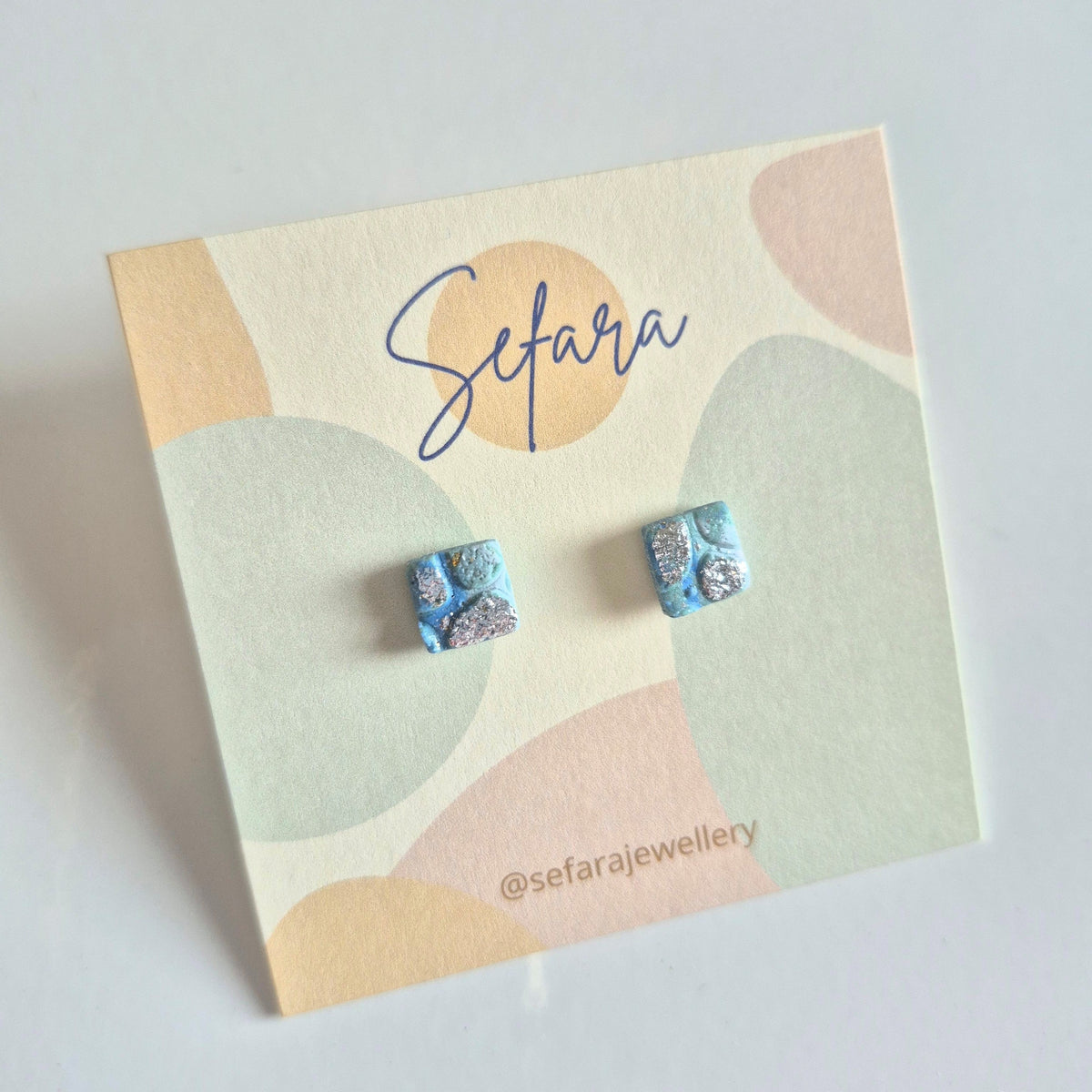 Blue square stud earrings with silver detail on a colourful card with Sefara branding