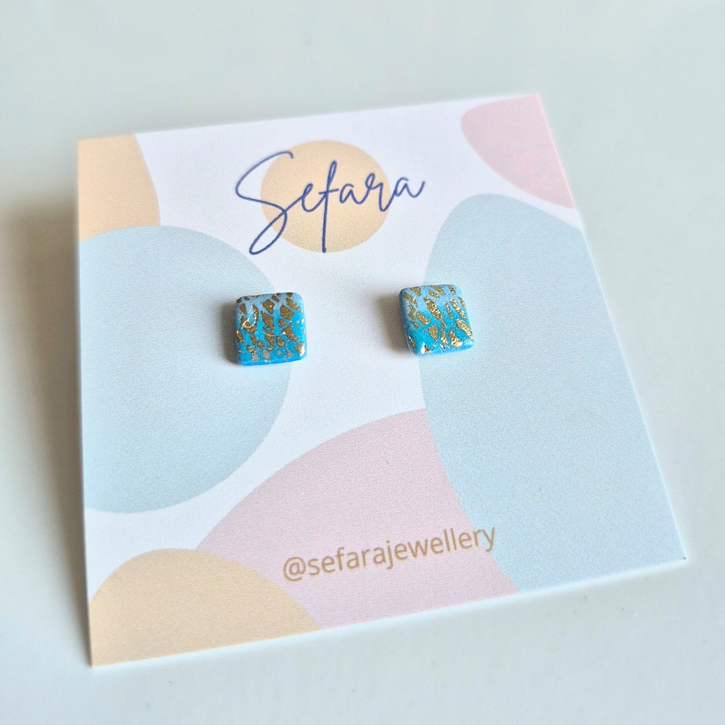 Turquoise square stud earrings with gold detail on a colourful card with Sefara branding