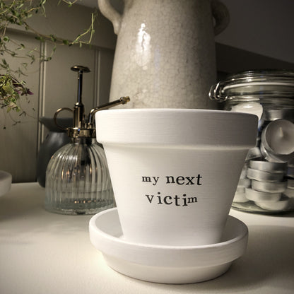 White painted terracotta pot with the text 'my next victim' on it, with matching saucer