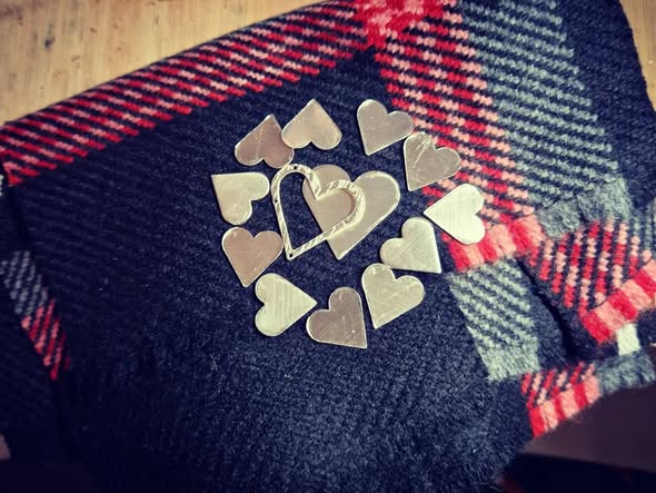 My Scottish Heart Silver heart-shaped pieces arranged in a circular pattern on a tartan fabric