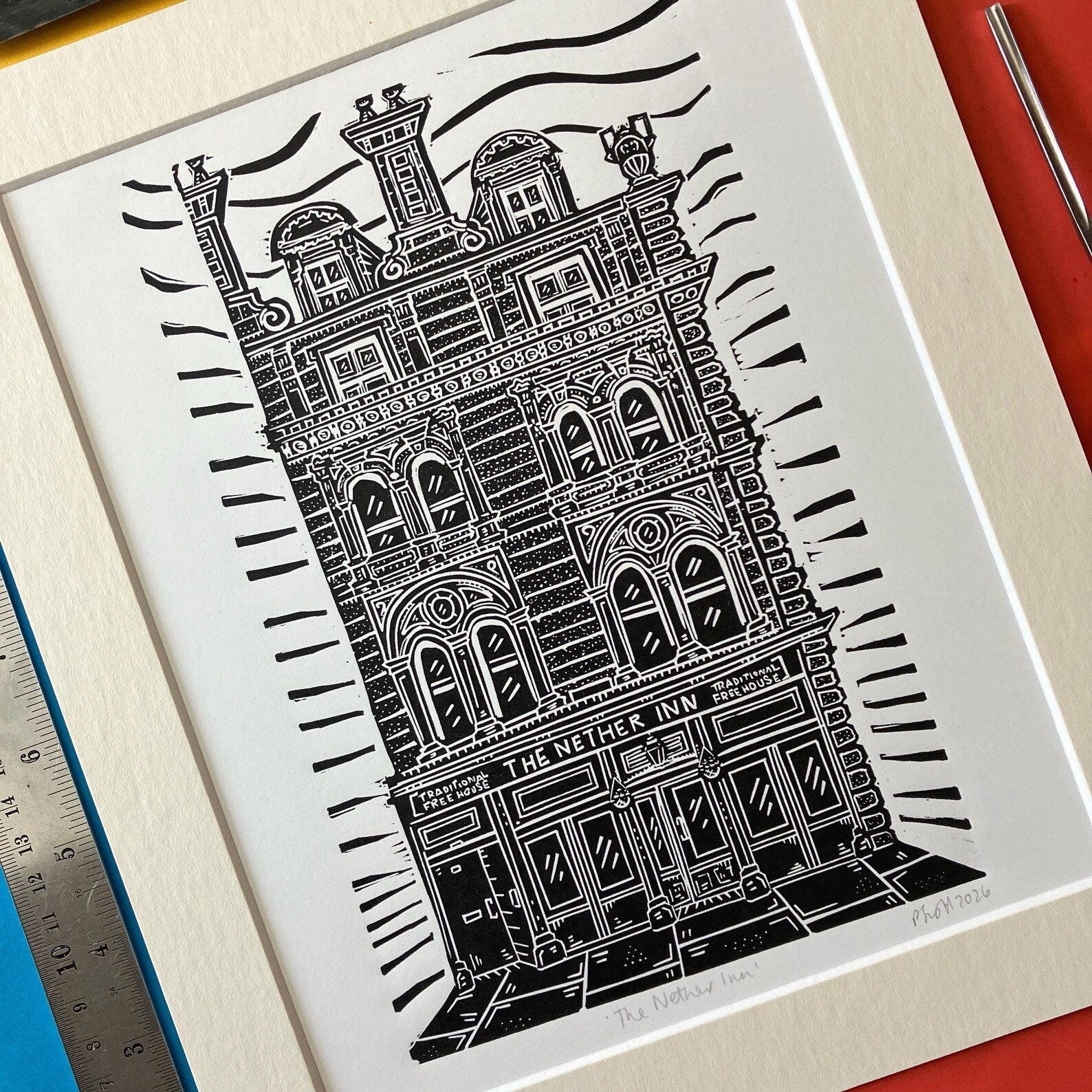 Framed black and white linocut print of The Nether Inn on a colourful background.