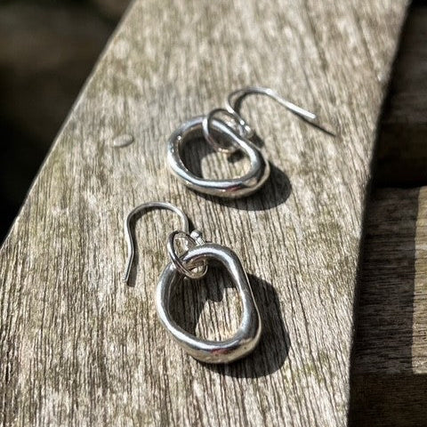 A pair of solid silver pebble drop earrings resting on a wooden surface.