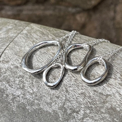 Four solid sterling silver pebble pendants of varying sizes (Small, Medium, Large, Extra Large) displayed on 18-inch silver chains.