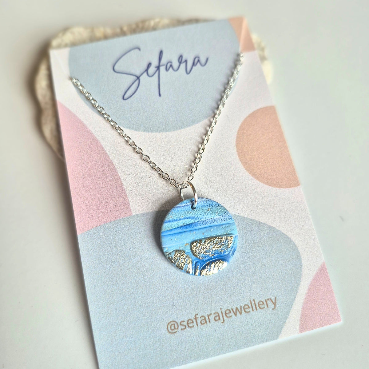 Blue Coastline round pendant necklace with gold leaf detail on a Sefara branded card