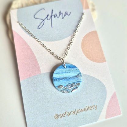 Blue Coastline round pendant necklace with silver leaf detail on a Sefara branded card