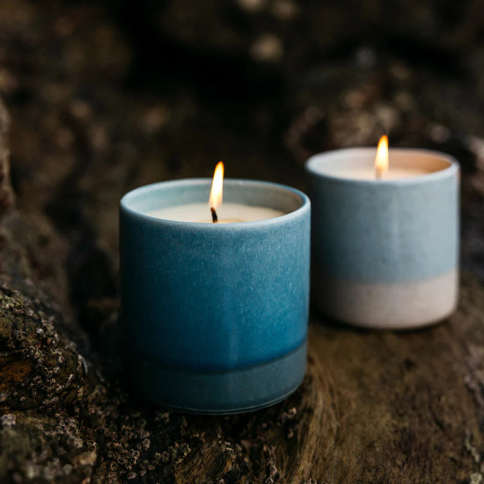 Two St Eval blue ceramic candles with flames on a dark background