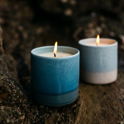 Two St Eval blue ceramic candles with flames on a dark background