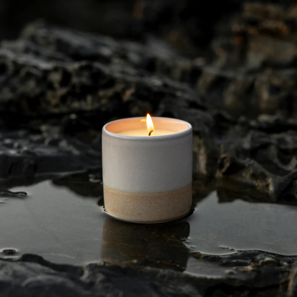 Cream and white St Eval ceramic candle holder with a lit candle on a dark, textured surface