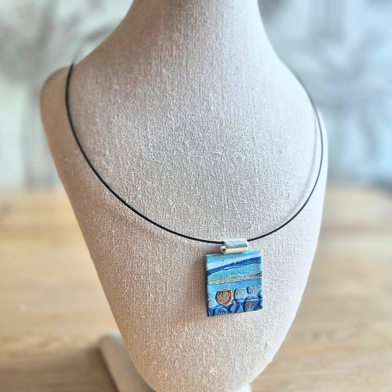 Sefara Jewellery coastal seascape pendant necklace with gold leaf detailing, featuring unique 30mm pendants on silver or black stainless steel chokers.