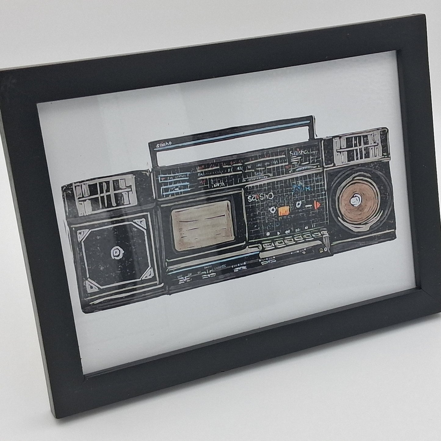 A colourful linocut print depicting a retro 1980s Saisho boom box tape recorder radio, mounted in a small black frame.