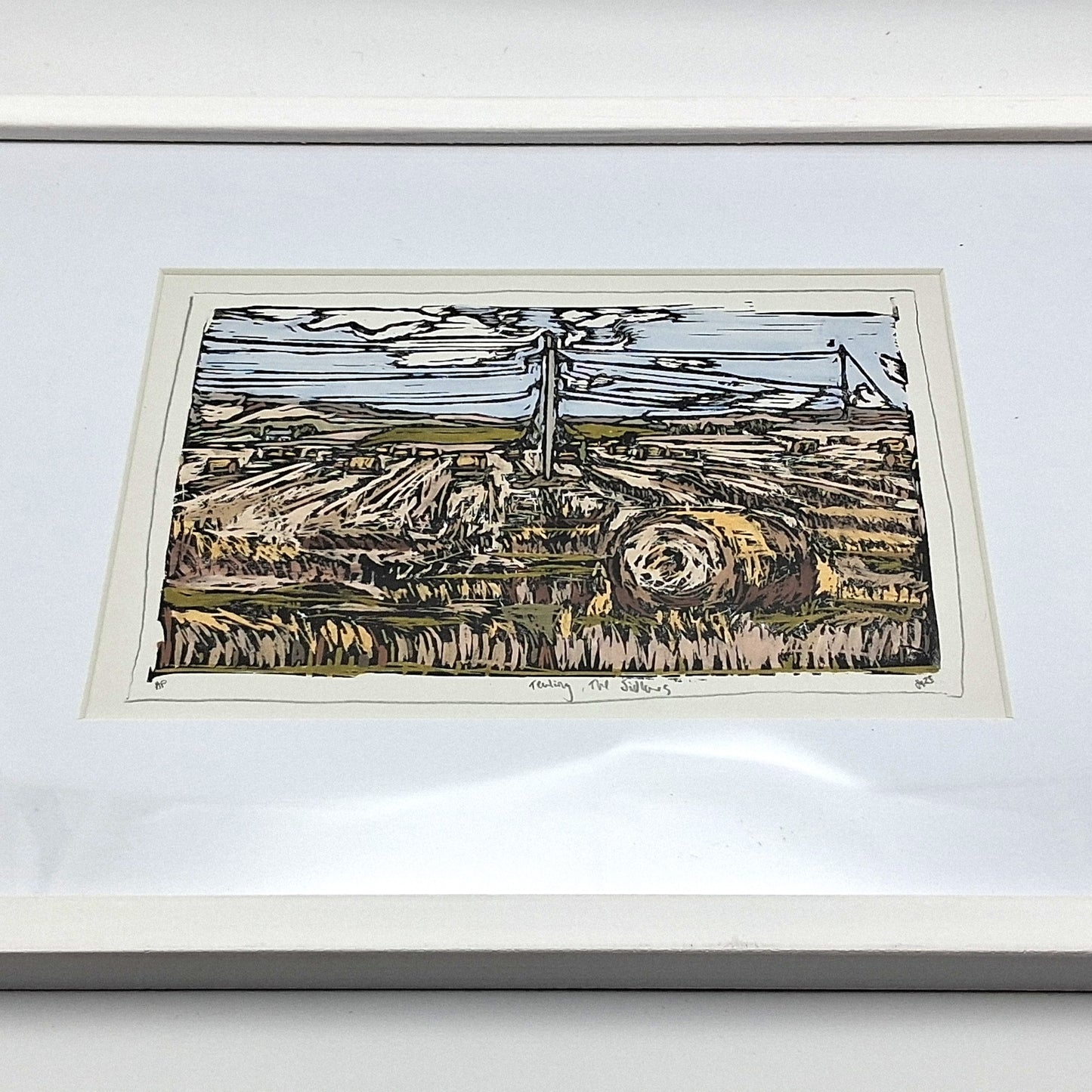 A colourful linocut print by BeeBirds depicting the rolling landscape of Tealing village nestled at the foot of the Sidlaw Hills in Angus, mounted in a white frame.