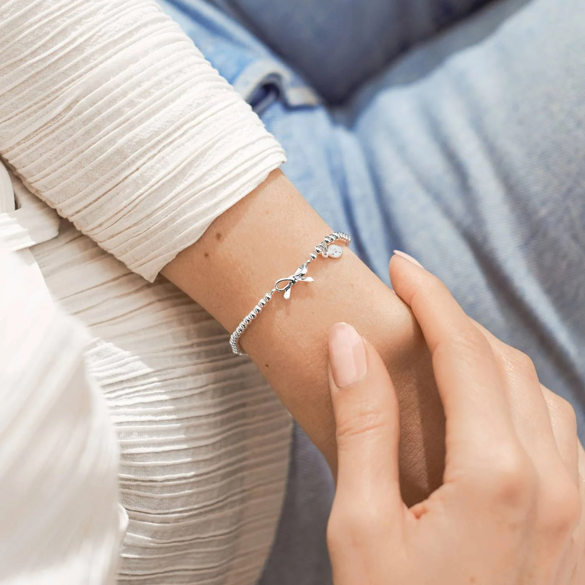 A silver Joma bracelet with a bow charm, packaged in a card that reads 'A Little THANK YOU'.