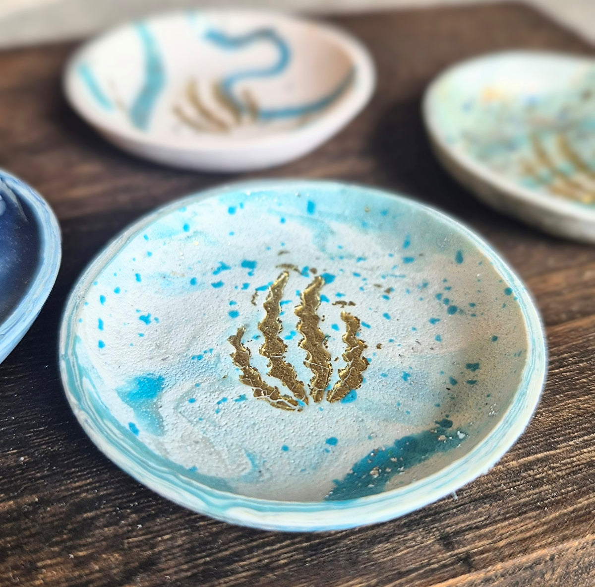 Sefara Jewellery handcrafted coastal trinket dishes featuring Scottish seascape colours and textures with gold leaf seaweed detailing, approximately 6cm in diameter.